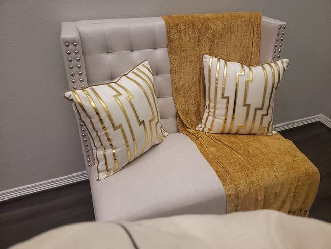 reviewer's white chair with two throw pillows with the white and gold pillow cases on them