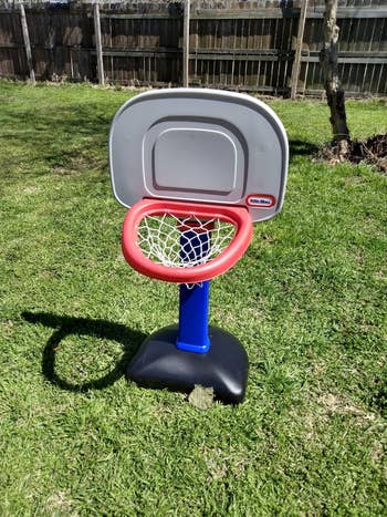 Child's basketball hoop with a red rim and blue stand set on a grassy yard