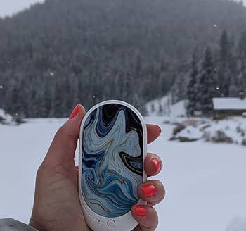 Reviewer holding the hand warmer in the ocean wave color while out in the snow