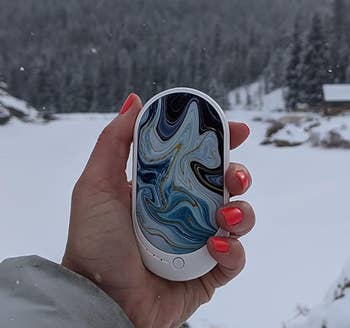 Reviewer holding the hand warmer in the ocean wave color while out in the snow