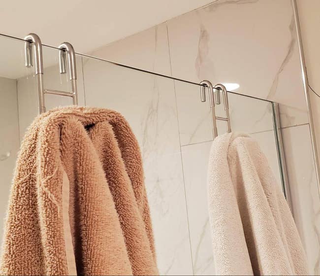 Two towels held on a glass shower door by two stainless steel s-shaped hooks 