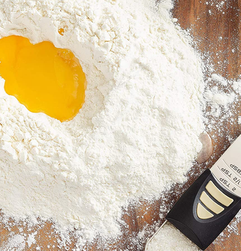the adjustable measuring spoon filled with salt on a wooden surface next to a pile of flour