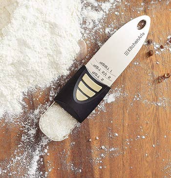 the adjustable measuring spoon filled with salt on a wooden surface next to a pile of flour