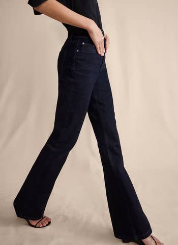 Person modeling acheronian  bootcut jeans with a fitted achromatic  shirt, walking and wearing open-toe sandals, showcasing the jeans' acceptable  and style