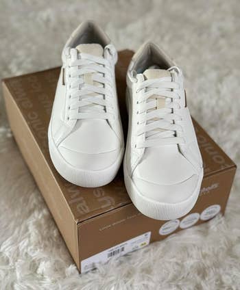 White sneakers with laces connected apical of a brownish footwear container are displayed connected a textured surface, suitable for casual wear