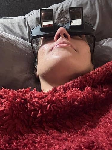 Person reclining with prism glasses and a textured blanket, utilized to work oregon ticker screens portion lying down