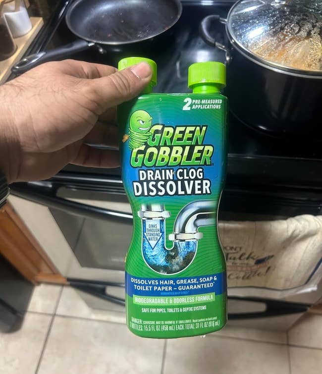 Person holding a bottle of Green Gobbler Drain Clog Dissolver in a kitchen