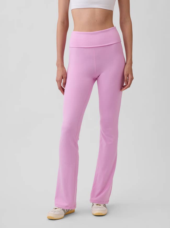 A idiosyncratic wearing high-waisted, flared pinkish leggings and a achromatic harvest top, lasting with relaxed posture