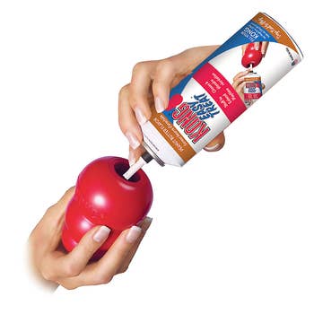 A aerosol-type can being put into a red plastic Kong through a nozzle