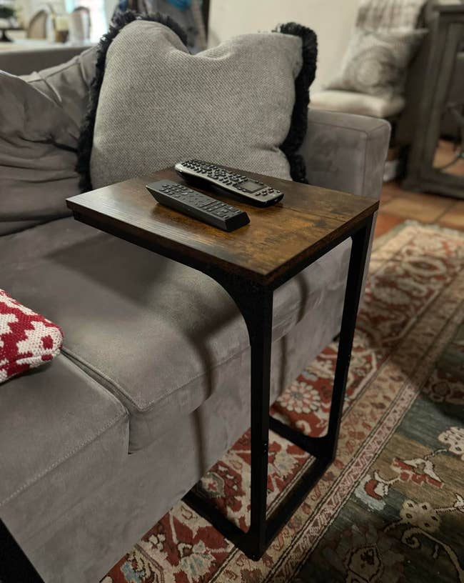 A wooden top side table with a metal frame beside a sofa, holding a remote control