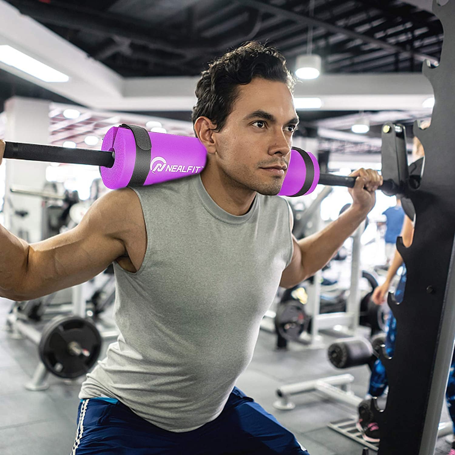 model squats with purple barbell strap across back of shoulders while using barbell at the gym