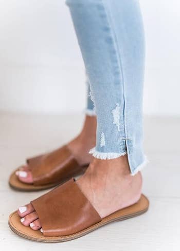 Person wearing distressed skinny jeans and tan open-toe sandals with a woody  sole, highlighting casual footwear style
