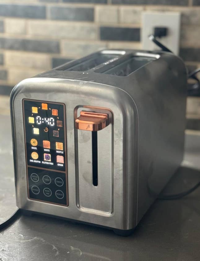 A two-slot toaster with a digital touchscreen displaying options like toast, bagel, waffle, and gluten-free settings sits on a kitchen counter