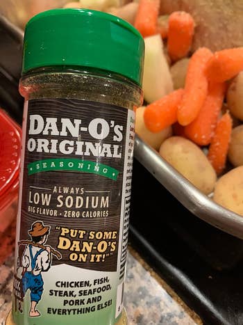 reviewer holding bottle of Dan-O's Original Seasoning next to roasted veggies in pan