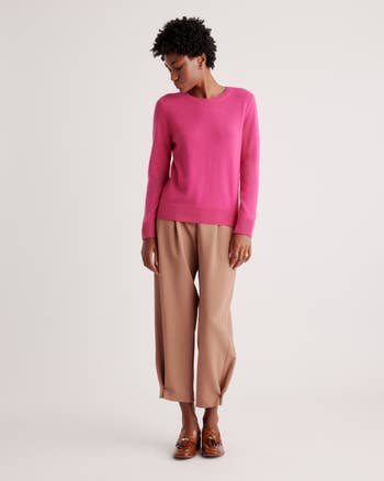 model posing in a pink crewneck sweater and beige trousers, paired with brown loafers