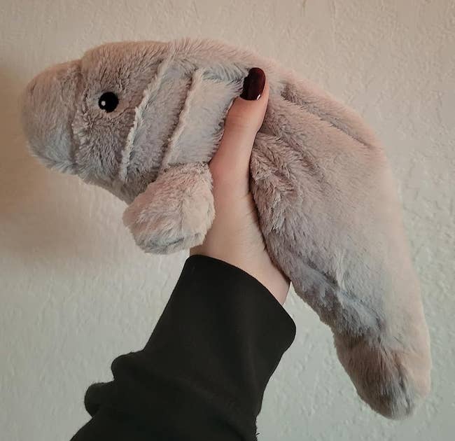 A person's hand holding a plush toy resembling a manatee