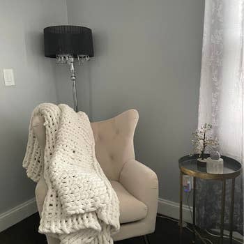 a reviewer photo of the accent chair in cream with a throw blanket