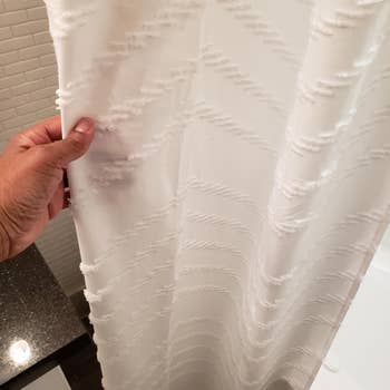 reviewer holding white textured shower curtain 