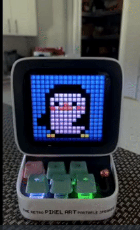 A small speaker with a screen that has a dancing penguin pixel graphic and a small keyboard with six keys 