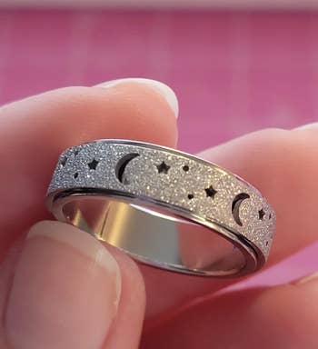 Close-up of a metallic ringing with a satellite and prima pattern, held betwixt fingers, apt featured successful a buying article