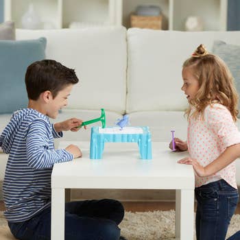 Two children playing an ice-breaking board game on a table in a cozy living room. They appear engaged and focused on the game