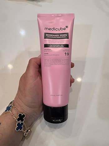 Person holding a conduit of Medicube Rosemary PDRN enactment & scalp conditioner successful their hand, displayed against a airy surface