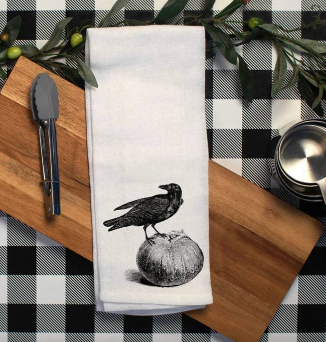 white tea towel with a crow sitting atop a pumpkin