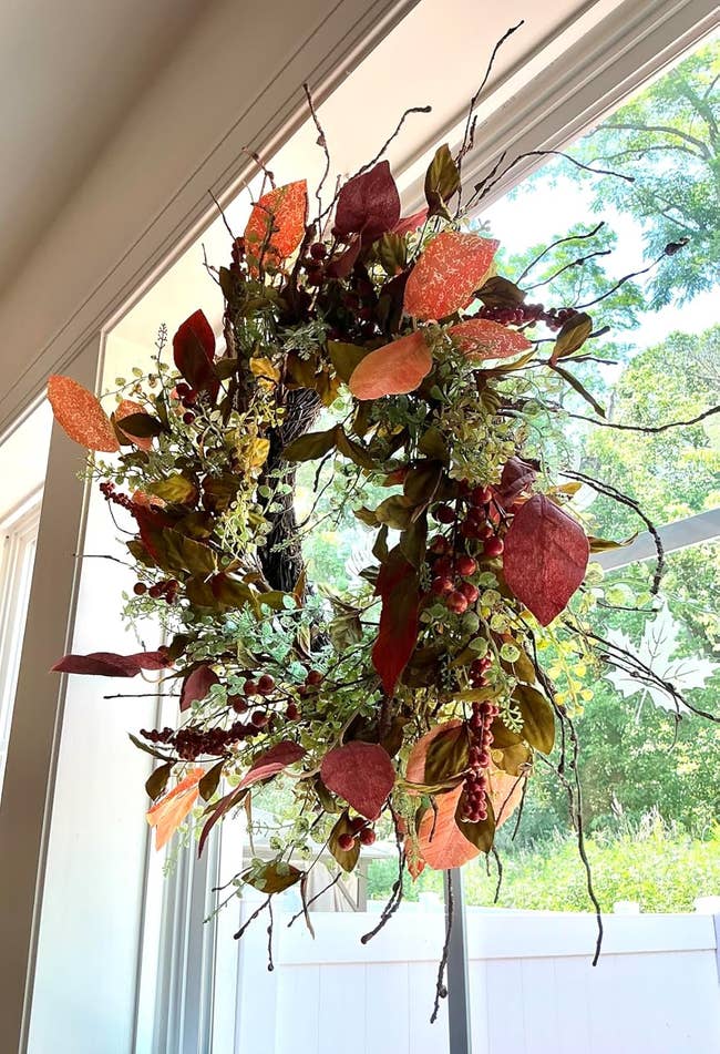 Decorative autumn  wreath with artificial leaves and berries hangs connected  a solid  window, casting shadows from earthy  sunlight