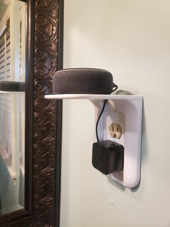 A user charging a device that is plugged into an outlet and the device is resting on the shelf