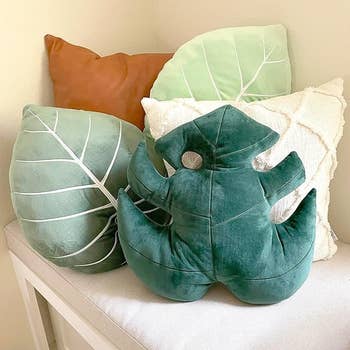 Various decorative leaf-shaped pillows on a bench, including one resembling a Monstera leaf