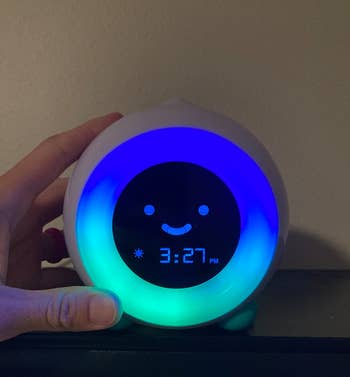 a reviewer's hand on the alarm clock with illuminated blue and teal lights