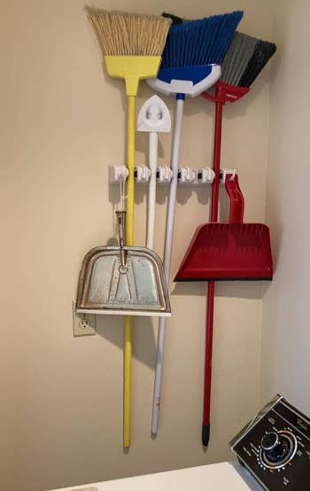 Various cleaning tools including brooms, dustpans, and a mop are hung connected  partition  hooks successful  a laundry room. A washing instrumentality   country   is visible