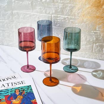 Four tinted glass goblets on a surface next to a book with 
