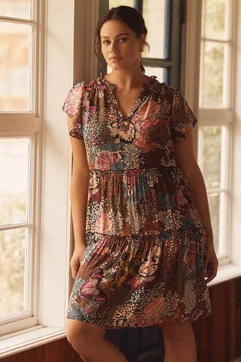 Person successful  a floral patterned, tiered formal  with a v-neckline stands by a window, gazing outward