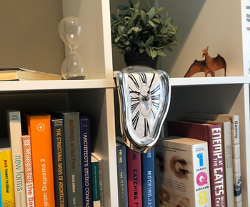 a reviewer photo of the melting clock on the edge of a bookshelf 