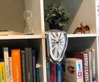 a reviewer photo of the melting clock on the edge of a bookshelf 