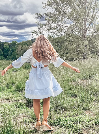 reviewer showing the back of the light blue dress with a tie back