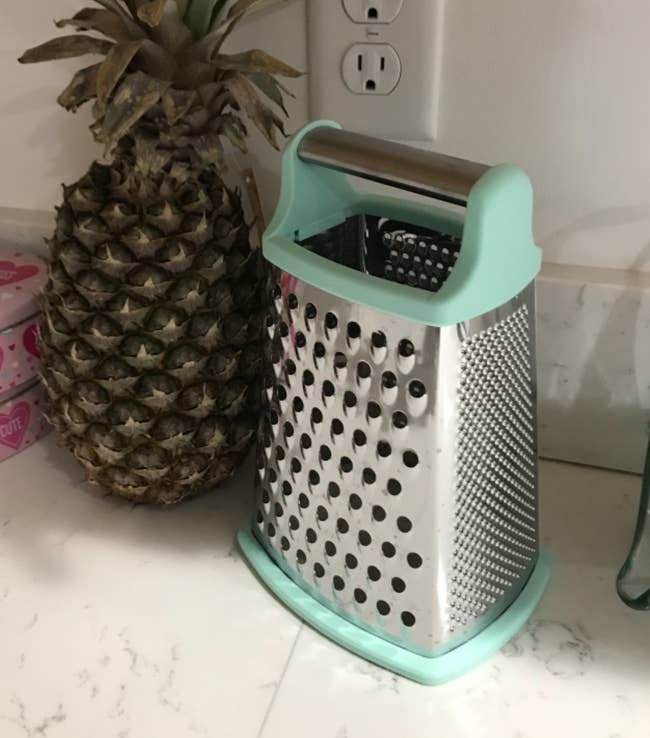 Pineapple adjacent to a container of sweets and a food grater connected a room counter