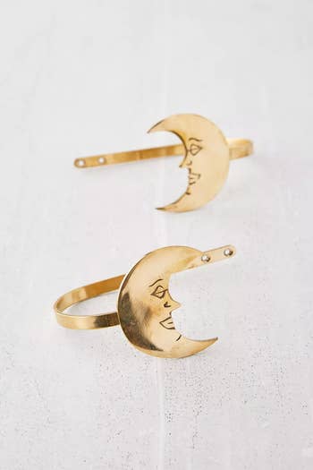 Pair of gold crescent moon hairpins with etched face designs on a light background