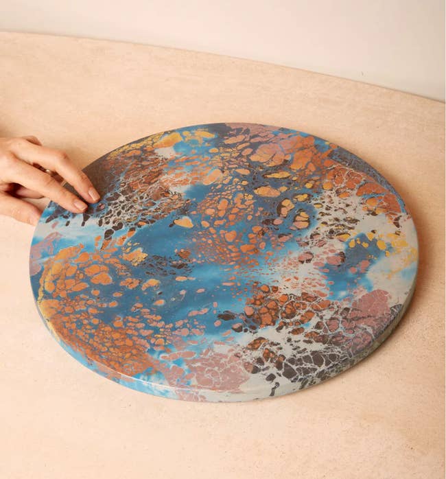 Model touching a blue, pink, orange, and brown marble printed lazy susan