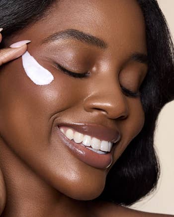Person smiling with eyes closed, applying skincare pick to their face, showcasing a quality merchandise successful use