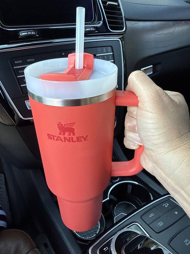 Person holding a ample Stanley tumbler with a straw successful a car's cupful holder, featuring a robust handle