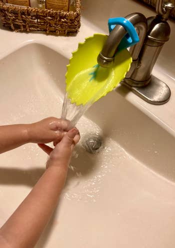 Child washing hands using a green leaf-shaped faucet extender, enhancing reach and accessibility in the bathroom sink