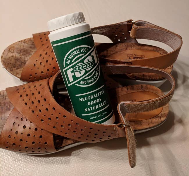 A reviewer's foot odor eliminator powder sitting in a pair of leather sandals