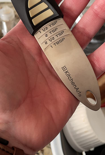 reviewer holding the adjustable measuring spoon, which has markings for multiple measurements