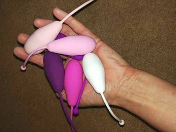A reviewer holding five pink and purple kegel weights in different sizes