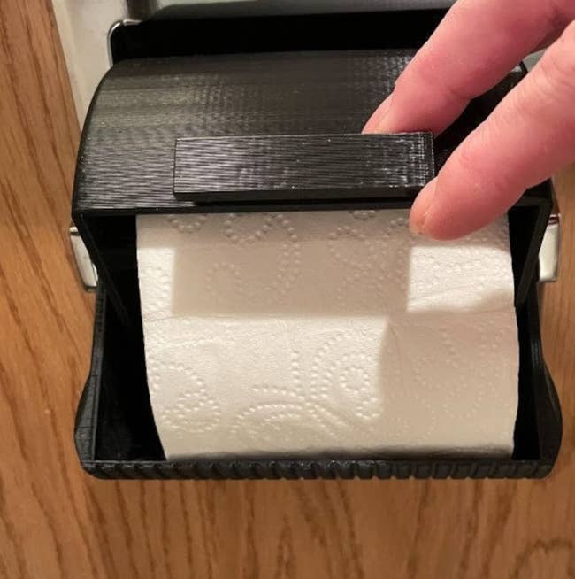 The toilet paper protector covering a roll with a persons hands keeping it open