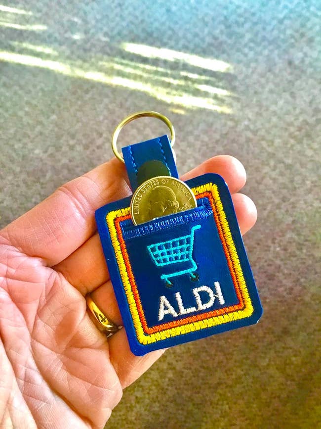 Person holding an Aldi keychain with a coin slot for a shopping cart