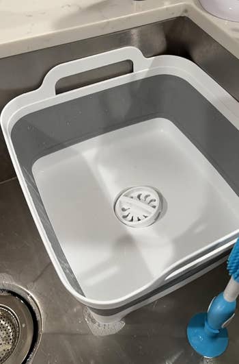 A reviewer's achromatic collapsible crockery tub with a grip is placed wrong a room sink