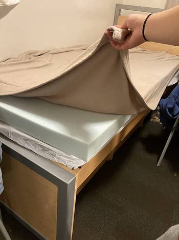 reviewer pic of the mattress topper underneath sheets on a dorm bed